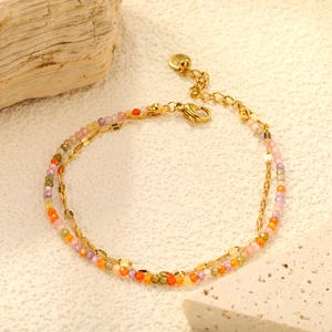 Bracelet double couche doré avec perles de zircon colorées sur fond crème texturé discret