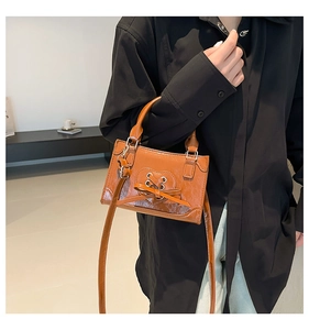 Detailopname van een karamelkleurige crossbodytas met hartstrik gedragen door model