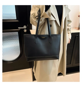 Detailed view of black leather tote bag worn by a model in a long beige trench coat