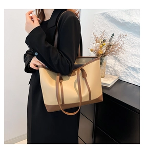 Detail of beige large tote bag with brown leather trim worn by model in black suit