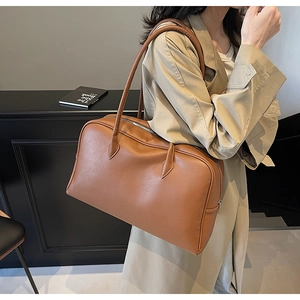 Detailed texture of brown pebbled leather Boston shoulder bag held by a model