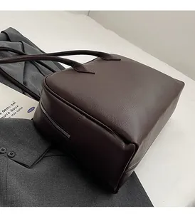 Detail of dark brown lychee leather texture and silver zipper on minimalist tote bag
