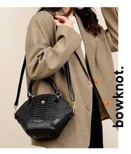 Détail du sac à main noir motif crocodile avec boucle abeille dorée porté par un modèle
