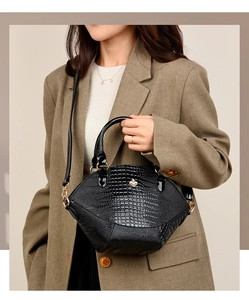 Détail du sac à main noir texture crocodile avec trèfle doré et poignée arrondie
