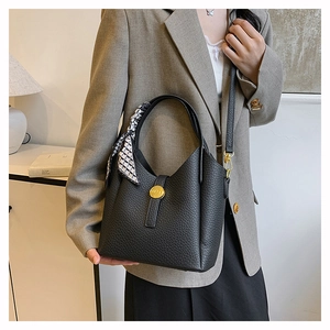 Detail of black lychee grain leather bucket bag with gold lock and geometric silk scarf