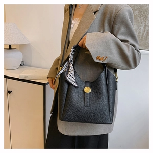 Detail of black pebble grain leather bucket bag with a decorative silk scarf and gold clasp