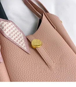 Close-up of pink lychee leather handbag with golden circular buckle and decorative scarf