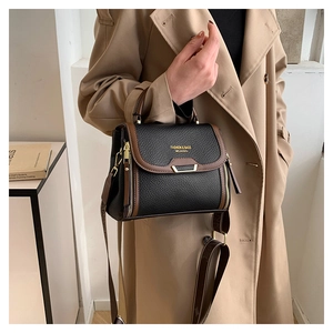 Detailed view of litchi grain leather handbag with wide strap worn with beige coat