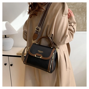 Black pebbled leather bag with brown trim and jacquard strap shown on a beige coat