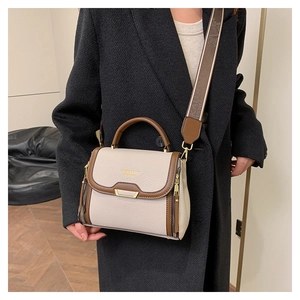 Close-up of cream textured leather handbag featuring broad jacquard shoulder strap and gold text