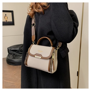 Detail of woman carrying a beige crossbody bag with brown trim and wide jacquard strap