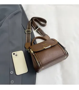 Detailed view of brown lychee leather handbag with wide jacquard strap and gold clasp