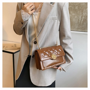 Detail of a brown quilted chain bag featuring a layered accordion structure and gold buckle
