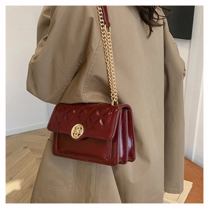 Close-up of wine red quilted faux leather shoulder bag with gold chain strap on model