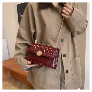 Close-up of burgundy quilted patent leather bag with a round gold metallic clasp and chain