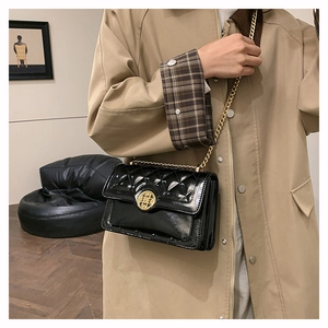 Detail of black quilted leather shoulder bag with vintage gold emblem buckle on trench coat
