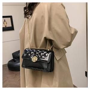 Detail of black quilted shoulder bag with glossy finish and gold chain strap