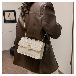 Detail of a beige quilted crossbody bag with gold chain strap worn with a brown leather jacket