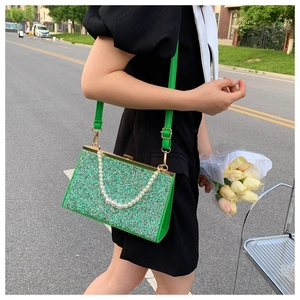 Detailed close-up of a green sequined handbag with a pearl chain and gold metal clasp