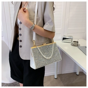 Silver sequin evening bag with large pearl chain on model wearing grey suit