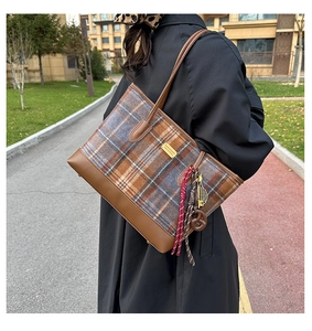 Détail du sac cabas en laine à carreaux avec garniture en cuir marron et pendentif décoratif