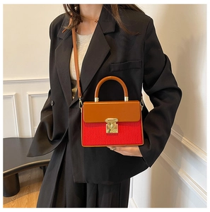 Detail of red and brown contrast handbag featuring a gold twist lock and sleek top handle