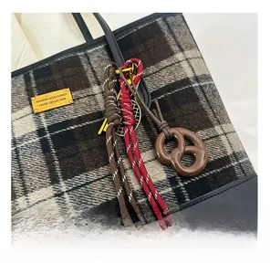 Détail d'un sac cabas en laine à carreaux avec bordure en cuir et breloque bretzel