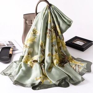 Detail of green silk scarf with yellow magnolia print draped over a leather bag