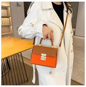 Detail of color-block box bag with orange pleats, brown flap, and gold lock clasp