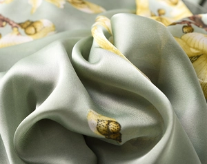 Macro shot of sage green silk fabric with magnolia floral print and glossy texture