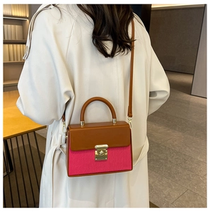 Brown and magenta leather crossbody bag shown on model with white coat in indoor setting