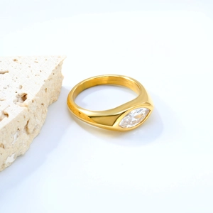 Dettaglio anello a fascia larga dorato con zircone marquise su sfondo in pietra bianca