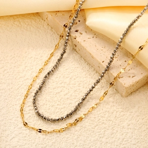 Double-layered 18K gold-plated chain and dark grey beaded necklace on stone