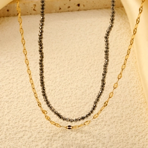 Double layered necklace with grey beaded strand and fine golden flat chain on stone background