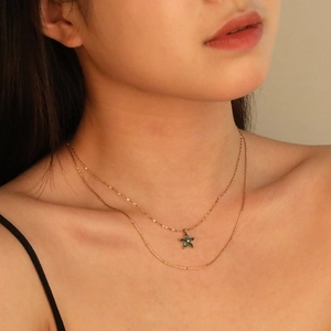 Elegant double-layered gold necklace featuring a sparkling green flower pendant on a model