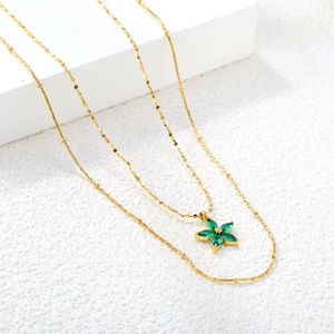 Close-up of double-layered gold necklace featuring a delicate green zircon flower pendant