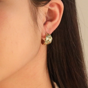 Irregular textured gold C-shape hoop earrings with small white stones on model