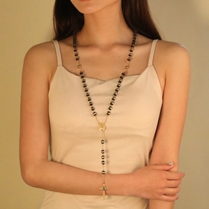Elegant beaded rosary cross necklace featuring black and gold beads on a model