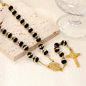 Detail of a gold and black beaded rosary necklace with a cross pendant and holy medal