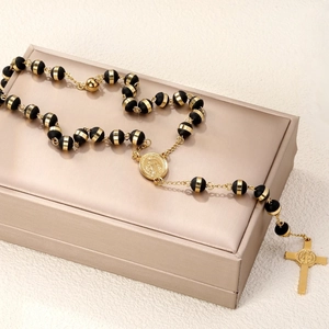 Detail of gold cross pendant and Saint Benedict medal on black beaded rosary necklace
