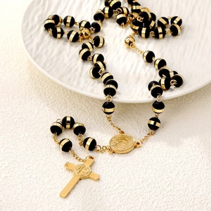 Cross pendant beaded necklace with black and gold rosary beads on white plate