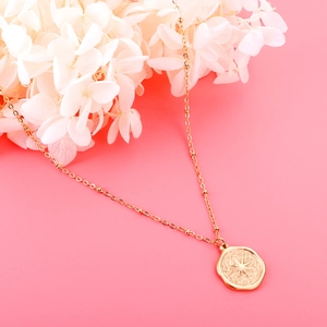 Close-up of golden coin necklace with starburst pendant and delicate beaded chain detail