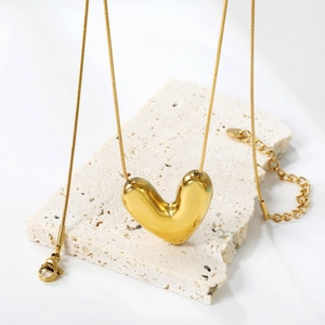 Gold heart pendant necklace with snake chain displayed on a textured natural stone