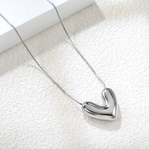 Detailed close-up of a high-polish silver heart pendant necklace on a minimalist surface