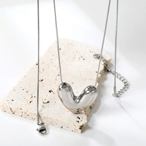 Polished silver heart pendant necklace on minimalist beige stone over white background
