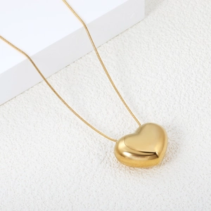Detailed view of polished gold puffed heart pendant with smooth snake chain necklace