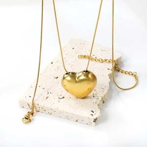 Macro view of polished gold heart pendant and snake chain on a textured stone base