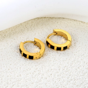 Close-up of gold hoop earrings with black enamel squares on textured surface