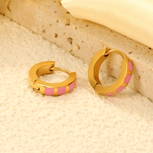 Detail of gold huggie earrings with pink enamel square inlay on a textured stone surface