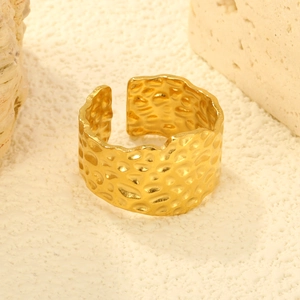 Bague large ouverte dorée avec texture martelée sur un fond de sable blanc artistique